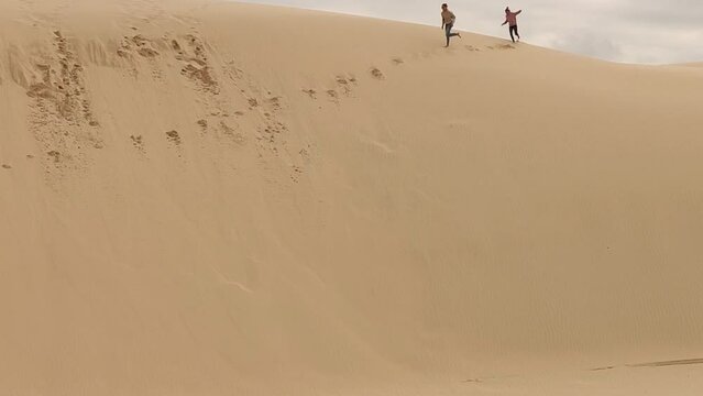 Young man and woman having fun running crossing the high sand dunes