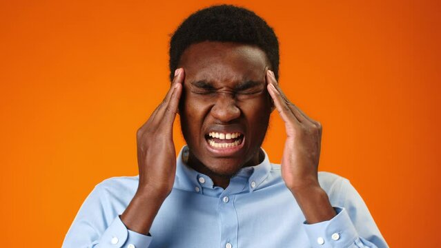 Young african man suffering from headache rubbing temples against orange background
