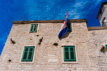 stone house facade with a hanging Croatia flag and green shutters