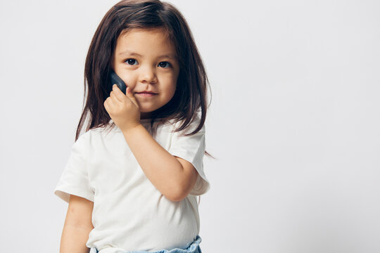 portrait of a cute, funny little girl in a white t-shirt talking on a smartphone with a very thoughtful face. Horizontal photo on a light background with empty space for an advertising layout insert
