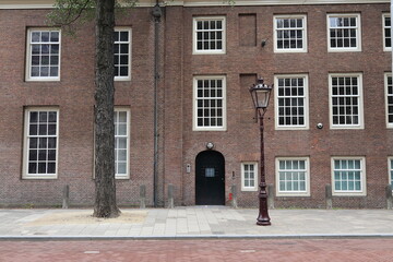 Fototapeta na wymiar Nieuwezijds Voorburgwal Street Building Facade with Windows, Door, Vintage Lamppost and Tree Trunk in Amsterdam, Netherlands