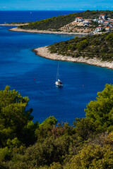 view from a bay with a sail boat, houses and buches in the foreground in Sevid, Croatia