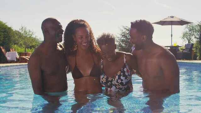 Portrait of smiling multi-generation family with adult offspring on summer holiday relaxing in swimming pool - shot in slow motion