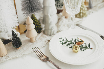 Stylish Christmas table setting. Cedar branch with bell on plate, vintage cutlery, wineglass,...