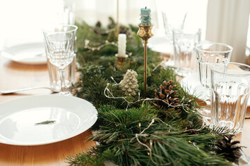 Christmas table setting. Rosemary branch on plate, vintage cutlery, candles, fir branches with golden lights and pine cones on table. Atmospheric Holiday arrangement