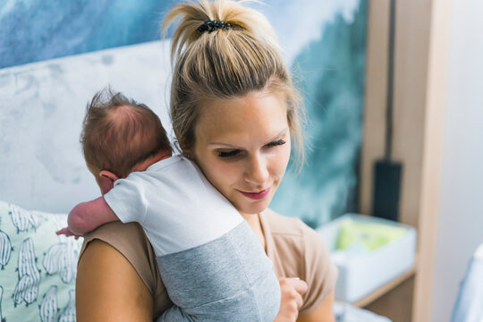 Forming bond between mother and her first-born child. Indoor closeup portrait of a young caucasian mother holding her adorable infant baby. Bedroom interior. High quality photo