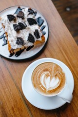 Toast with whipped cream and oreo topped with capuchino coffee in white plate on a wooden table