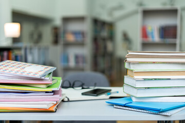 Book stack on wood desk and blurred bookshelf in the library room, education background, back to school concept