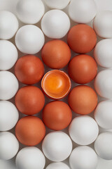 Row of white and brown eggs and single broken egg with a yolk. Mosaic pattern of brown and white whole eggs and cracked brown egg with a yolk. Flat lay