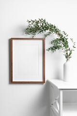Portrait frame mockup for artwork on white wall with natural eucalyptus twigs.
