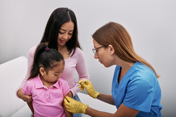 Korean girl and her mom during vaccinated by general practitioner in doctor's office. Child's...