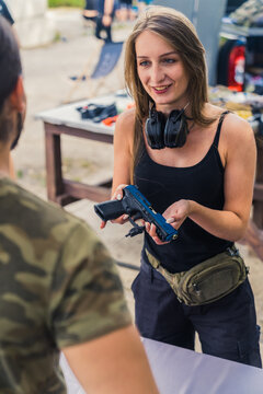 cowboy shot of a young Caucasian woman holding a gun and talking to her instructor at the shooting range. High quality photo