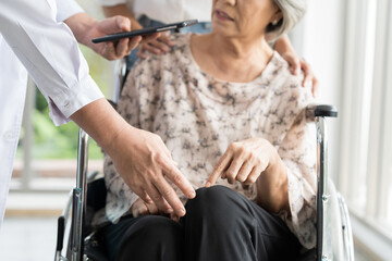 Male doctor taking care and checking up knees elderly female on wheelchair at the hospital. People and health care concept