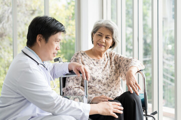 Male doctor taking care and checking up knees elderly female on wheelchair at the hospital. People and health care concept