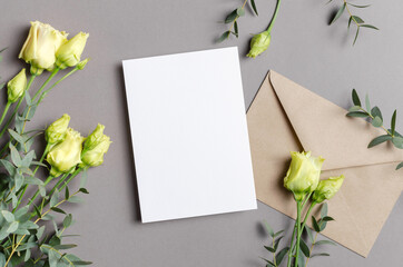 Blank invitation or greeting card mockup with eustoma flowers and craft envelope on grey