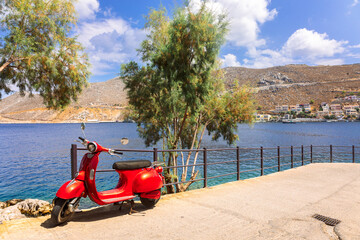 Old red scooter is parked on waterfront of beautiful island of Symi. Colorful summer landscape with city view. Symi, Greece. High quality photoOld red scooter is parked on waterfront of beautiful © lara-sh