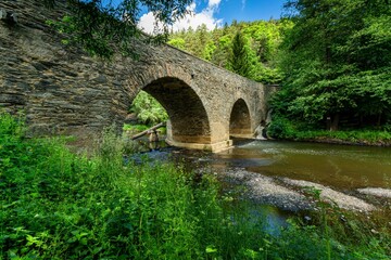 Rabstejn nad Strelou, Czech Republic - June 12 2022: View of the historical sandstone bridge over the river Strela made in the 14th century, a second oldest in the Czech Republic. Sunny summer day.
