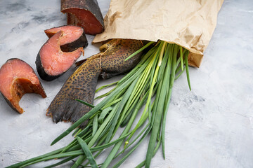 hot smoked fish in a craft bag with green onions with chopped pieces on a light background macro photo
