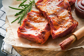 Pork ribs. Raw meat. Raw pork ribs in marinade with spices, rosemary, tomato sauce and garlic on old wooden stand on black stone table background. Barbecue concept. Top view. Mock up.