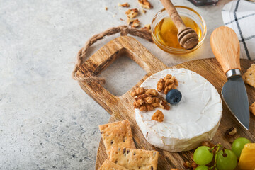 Assortment of cheese, honey, cracker, blueberries, grapes with red and white wine in glasses antipasto server on white marble board on grey background. Cheese plate. Flat lay, copy space.