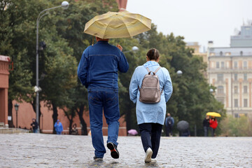 Rain in Moscow, couple with one umbrella walk on a street. Rainy weather in autumn city