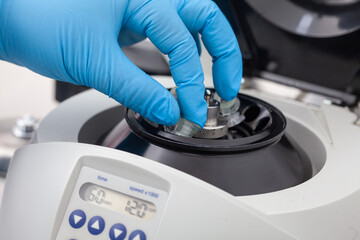 Closeup of a scientist hand placing a tube into an small table centrifuge. Spin column-based nucleic acid purification technique.