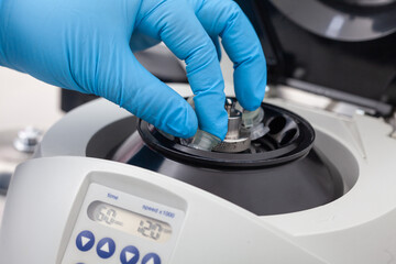 Closeup of a scientist hand placing a tube into an small table centrifuge. Spin column-based...