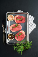 Steaks. Fresh Filet mignon Steaks with spices rosemary and pepper in kitchen tray on light gray background. Top view.