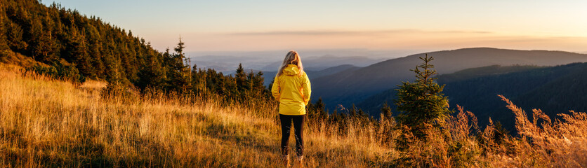 Woman looking at mountain range in natural parkland Jeseniky during sunset. Panoramic landscape...