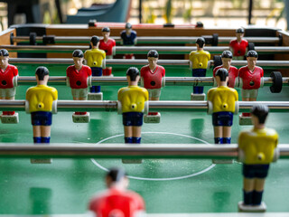 A vertical close-up view of a typical foosball table with red and yellow dummies over a green surface simulating a soccer field.