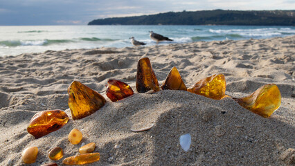 Orange Baltic amber stones on the sand against the sea.  
Amber jewelry.