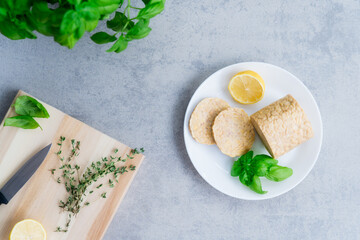 Top view raw Tempeh or Tempeh, made of fermented soybean seeds. Tempeh Slices on plate with herbs. Soya protein. Plant based meat concept. Healthy Cooking and eating. Go vegan. Flat Lay, copy space