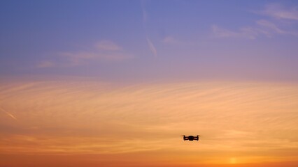 Fototapeta na wymiar The drone takes off into the sunset sky over an unrecognizable place. A beautiful sky filled with sunset colors in which a drone flies with blinking lights. Four propellers lift the drone into the air