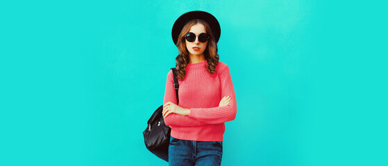 Portrait of beautiful young woman wearing black round hat, sweater on blue background