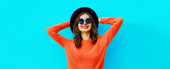 Portrait of beautiful smiling young woman wearing black round hat, sweater on blue background