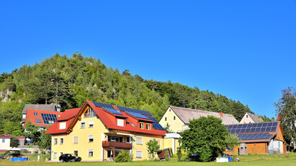 Wohnhäuser mit Solaranlagen zur Nutzung der Sonnenenergie vor Berg und blauem Himmel