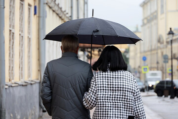 Rain in city, couple with one umbrella walking on a street. Rainy weather in autumn
