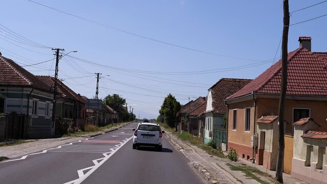 The car is driving on a narrow road in a small village.