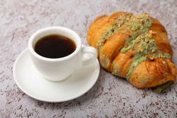 Aromatic coffee in a cup with pistachio croissant on a textural background.Espresso. Morning drink. Breakfast. Cheerful morning concept. Place for text. Place to copy.