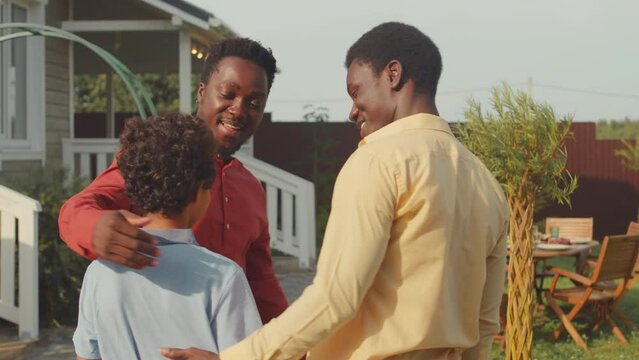 Medium Shot Of Two African American Grown Up Brothers Or Male Friends And 11 Year Old Son Of One Of Them Meeting For Dinner At House Yard On Warm Sunny Day