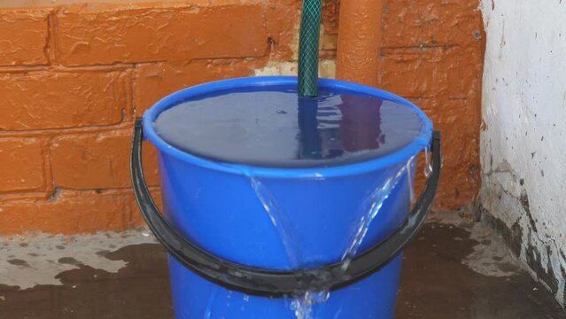 The water from the hose has filled the bucket and is overflowing