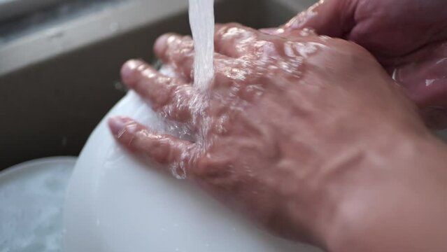 A man washes a white plate with a sponge.
