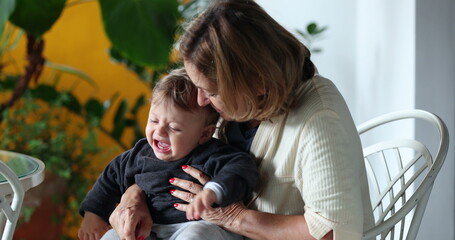 Grandmother holding crying baby grandson. Grand-parent trying to console tearful infant child