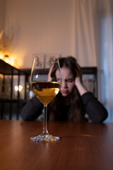 Young woman sitting in the kitchen with a glass of wine. Teen alcoholism concept, alcohol addiction problems among women