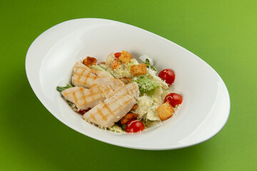 Salad with chicken and tomato in a plate on a green background.