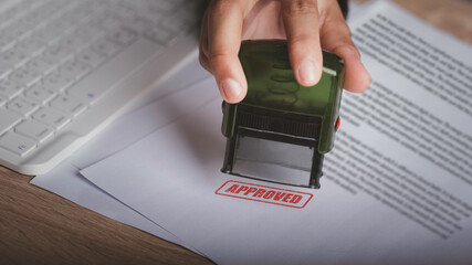 Approved stamp concept. Close-up Of A Person's Hand Stamping in paper contract, loan or certificate document at desk. Businessman clerk data paperwork before agreement important job. - obrazy, fototapety, plakaty