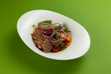 Salad with pieces of beef in a plate on a green background.