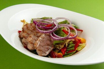 Salad with pieces of beef in a plate on a green background.
