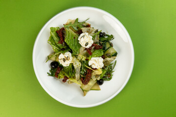 Salad with cucumbers and sun-dried tomatoes in a plate on a green background.