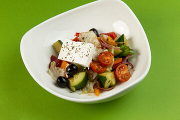 Greek salad in a plate on a green background.